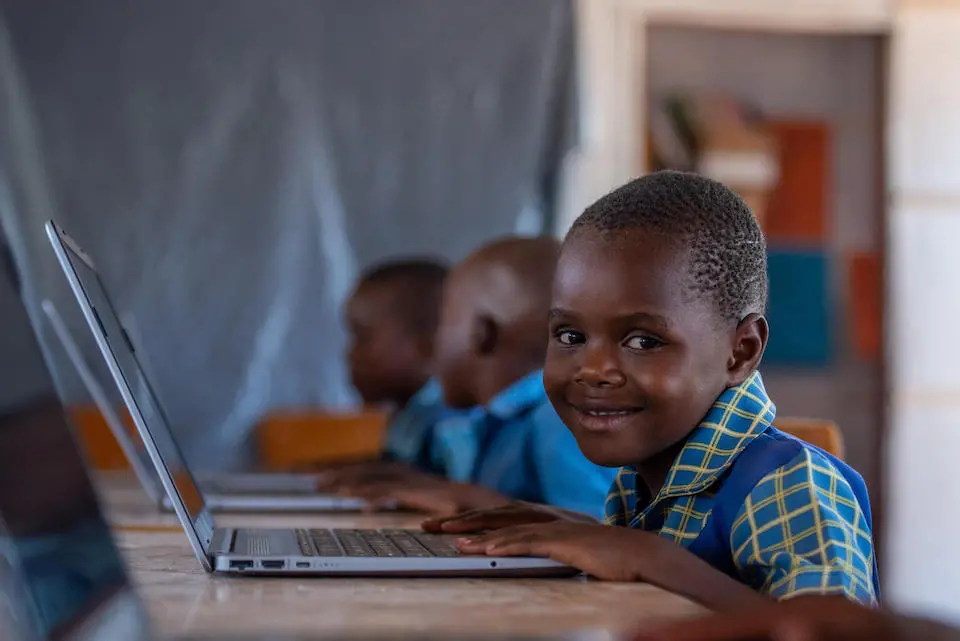 A student smiles while using a laptop to access online education in Zimbabwe, supported by the Giga initiative.