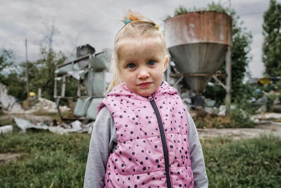Milana, 4, stands in front of the destroyed boiler room at her kindergarten in the village of Mala Rohan, in the Kharkiv region of Ukraine.