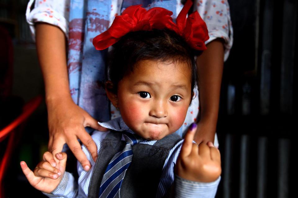 A young girl displays her inked little finger as a mark to show that she just got vaccinated during UNICEF-supported measles, rubella and polio vaccination campaign conducted at Barpak village health post in Gorkha district, Nepal.