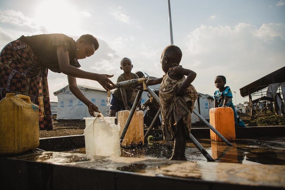 A mother draws water with her young daughter from a tap funded by the European Union through UNICEF at the Bushagara camp for internally displaced persons in eastern DRC on Aug. 24, 2023.