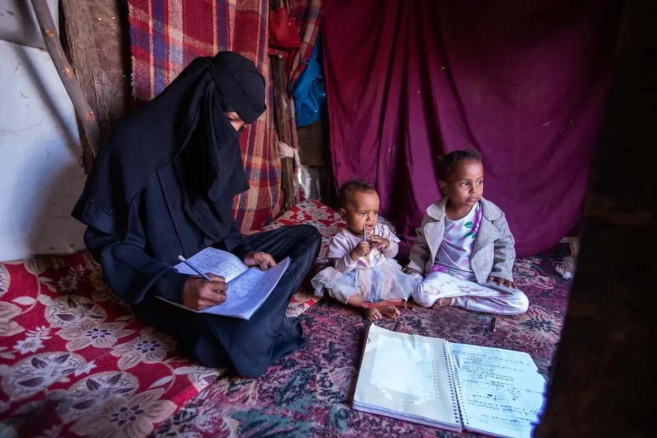 Yousra, 16,does homework for her UNICEF-supported literacy and numeracy classes with her young daughters by her side in Taizz, Yemen.