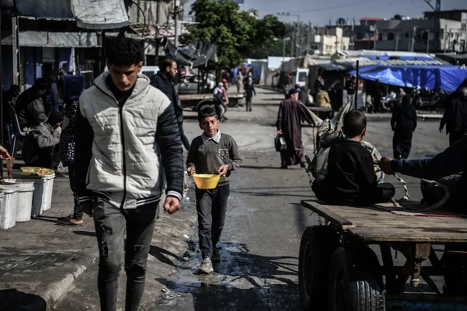 Muhammad, 11, carries a bowl of beans to his family's tent in Rafah, southern Gaza.