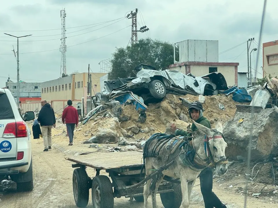 On March 219, 024, a young man standing next to a donkey-pulled cart looks on as a convoy of UNICEF vehicles travels on a street in Khan Younis, southern Gaza Strip.