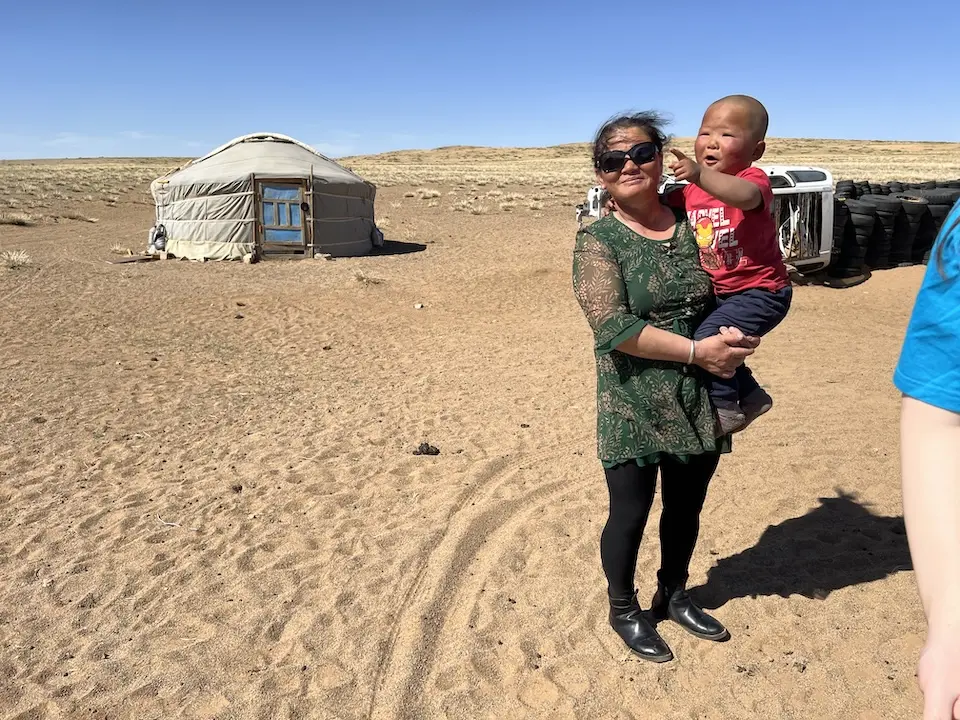 In Dundgobi province, south-central Mongolia, a mother holds her 3-year-old son outside the family home, a traditional ger, or tent, which the family will soon break down, pack up and load onto a truck to relocate to a new location where the animals will find better grazing.