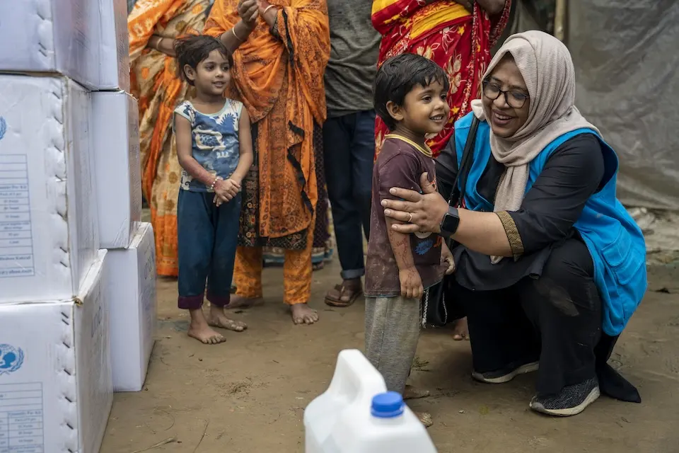 UNICEF staff member kneels beside a child affected by the flooding in North-East Bangladesh at a distribution point for emergency supplies.