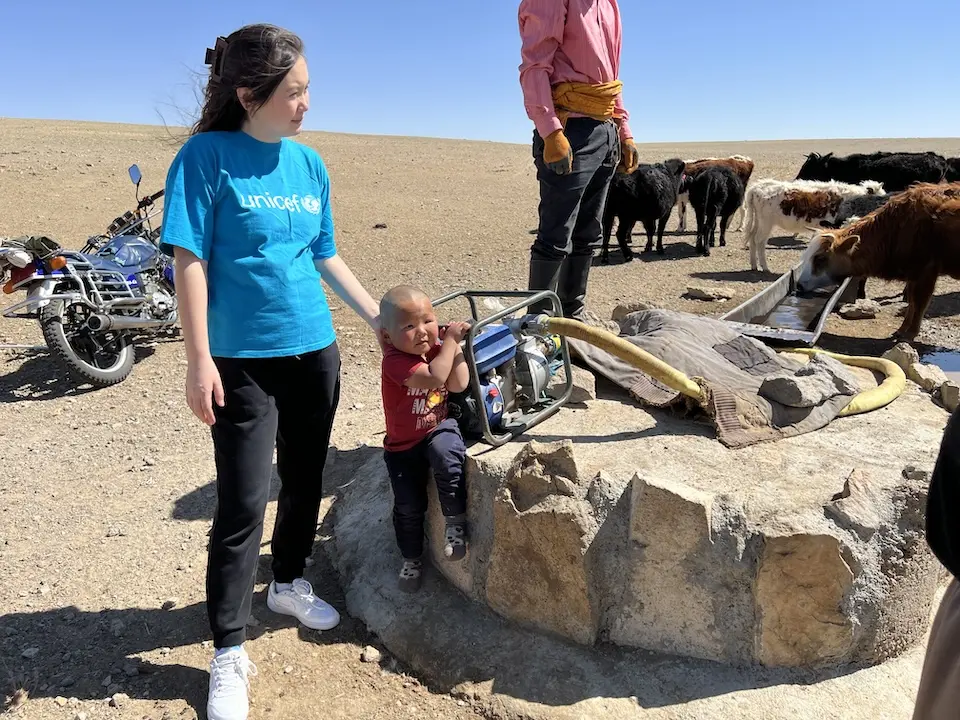 Nominzul Tumurjav, Digital Communication Officer for UNICEF Mongolia, supports 3-year-old Ochir-erdene, son of herder Och Erdene of Dundgobi province, by the well they use to water their livestock.