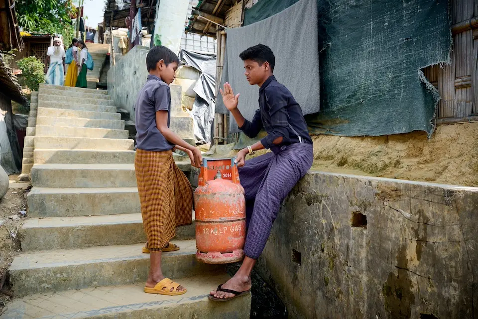 Anayet, 15, an adolescent peer leader, speaks with a boy, a fellow Rohingya refugee who is carrying a heavy gas cylinder, about the harmful effects of child labor.