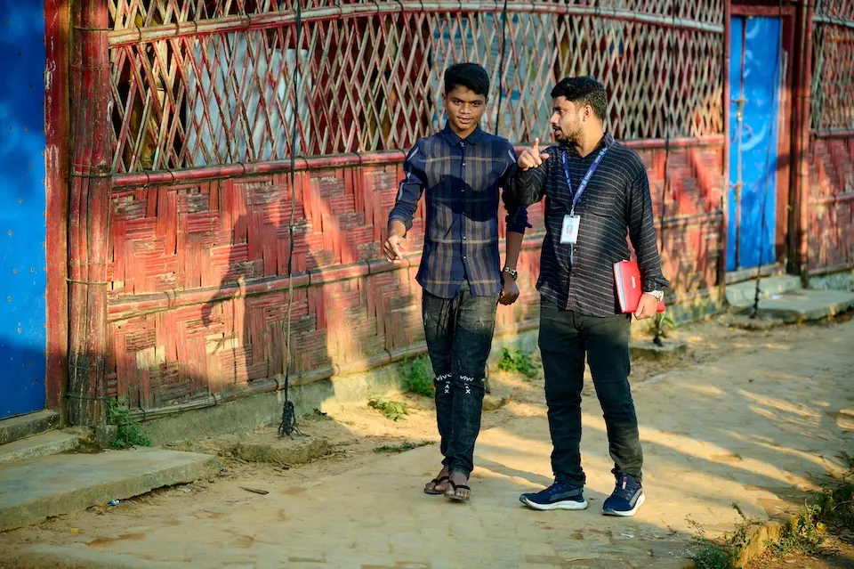 On 7 Nov. 7, 2023, Anayet, 15, an adolescent peer leader, walks with case worker Salauddin in the Rohingya refugee camps in Cox’s Bazar, Bangladesh.