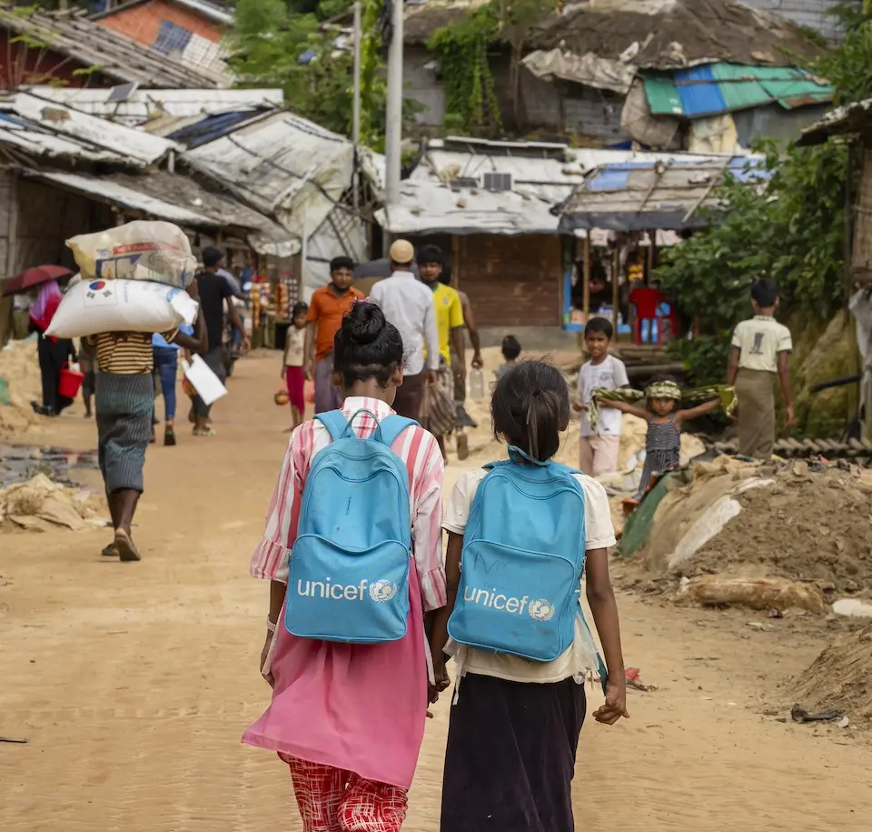 On July 15, 2024, two girls with UNICEF backpacks walk down a main road in the Rohingya refugee camps in Cox’s Bazar, Bangladesh.