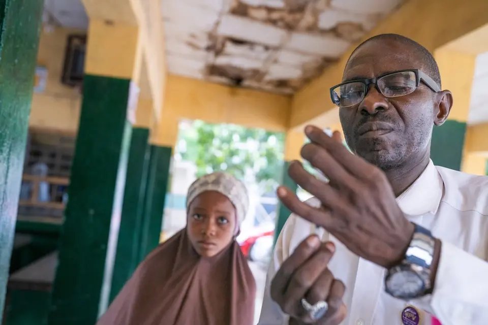 Safiyya, 10, watches as Alimudeen Mohammed, ward in charge at the Katsina Kofar Marusa Maternal and Child Health Clinic, prepares a human papillomavirus (HPV) vaccine in Katsina, Nigeria on May 30, 2024.