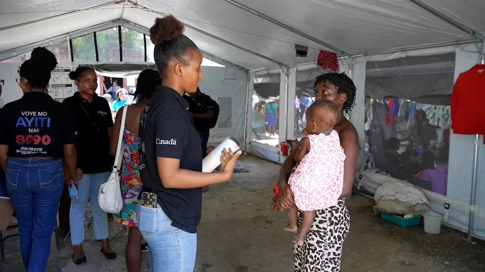 A young UNICEF U-Reporter shares health information with a mother holding her child in Port-au-Prince, Haiti.