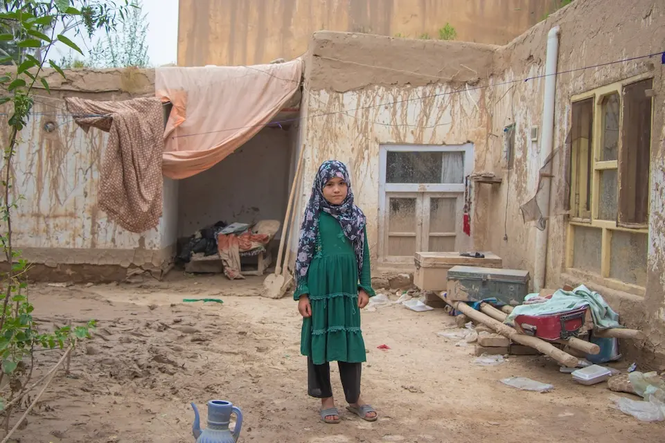 Ten-year-old Hosna stands outside her house, which was damaged during recent flash floods in Baghlan province, Afghanistan.