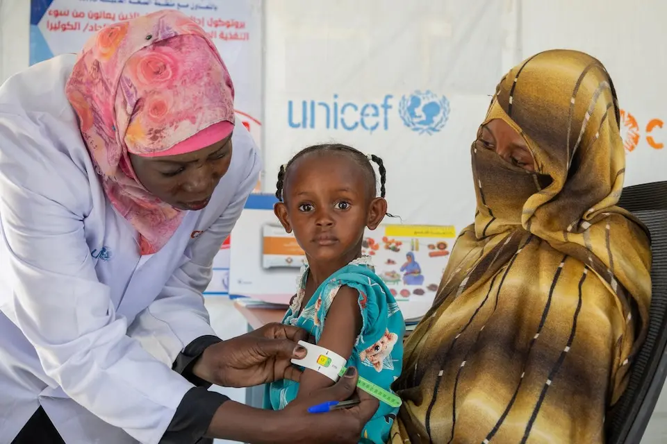 Sitting on her mother's lap, a little girl is screened for malnutrition at the UNICEF-supported Alkarama clinic in Kassala state, Sudan.