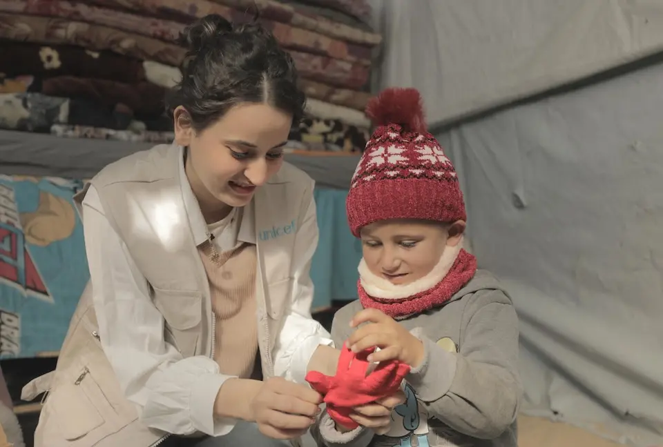 On Dec. 28, 2024, a UNICEF staff member helps a child try on warm winter clothes, part of a winter kit distributed to children in Al Fajer Camp, Khan Younis, South Gaza.
