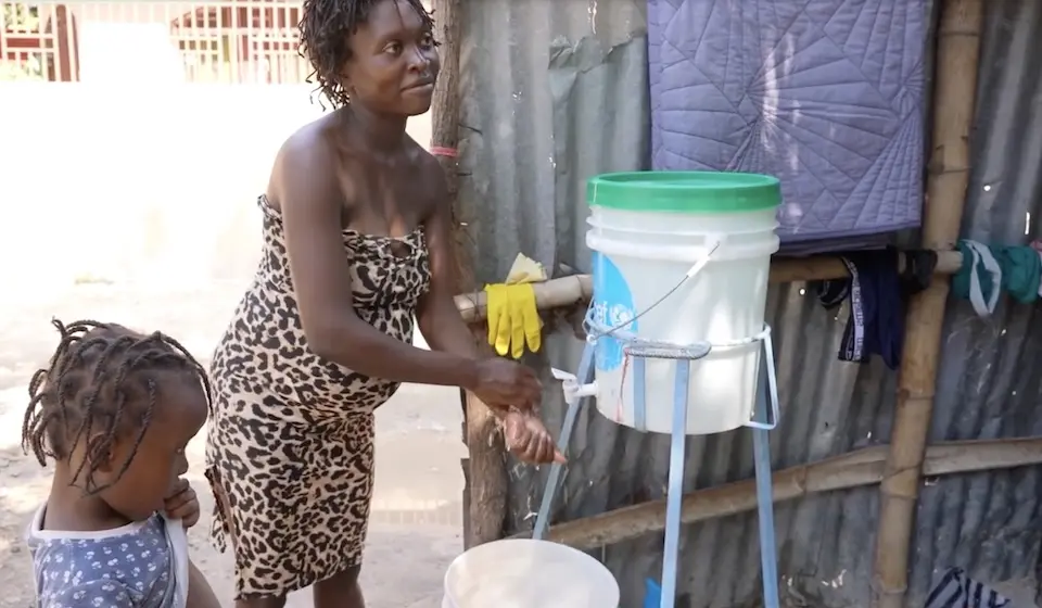 At the Jean Marie Cesar school, an internal displacement site in Port-au-Prince hosting 3,000 people uprooted by violence, a pregnant mother fills a bucket with safe drinking water from a source supplied by UNICEF while her child stands by watching.