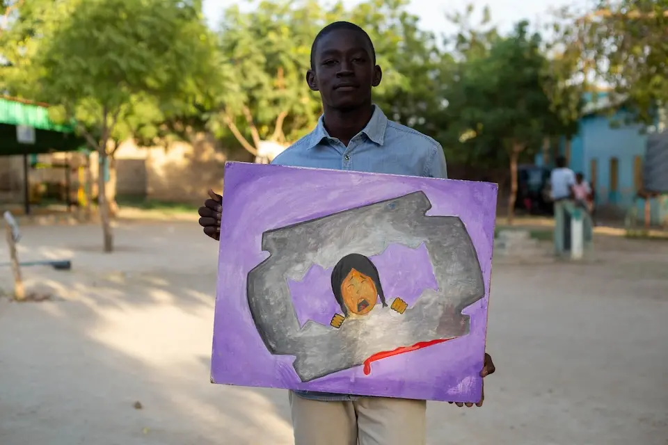 In Sudan, Moataz, 17, holds a painting he made to show the harm caused by female genital mutilation.