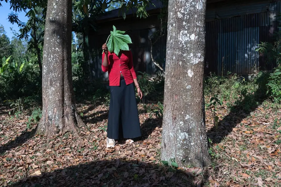 A young woman who was subjected to female genital mutilation at the age of 11 stands between two trees in Ethiopia, a leaf covering her face to protect her privacy..