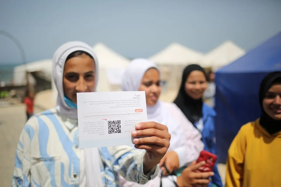 Adolescent girl in Rafah, the Gaza Strip, holds the QR code she can scan to provide feedback on the adolescent girls care and protection supply package distributed by UNICEF and partners.