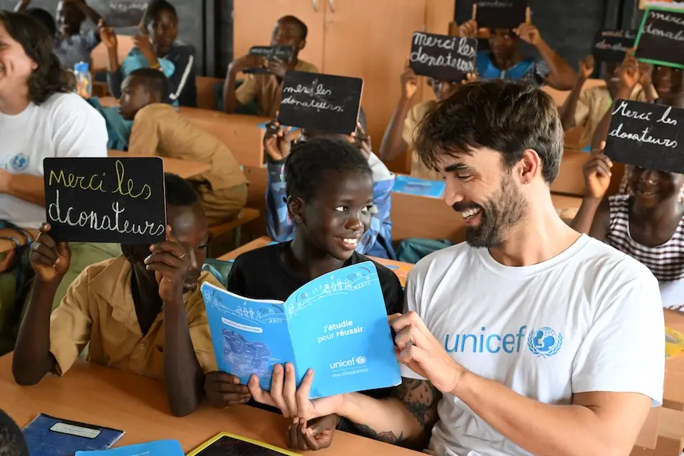 A staff member from UNICEF Spain sits with students inside a classroom during a program visit to public primary school EPP HKB Domoraud, in Man, western Côte d’Ivoire in October 2024.