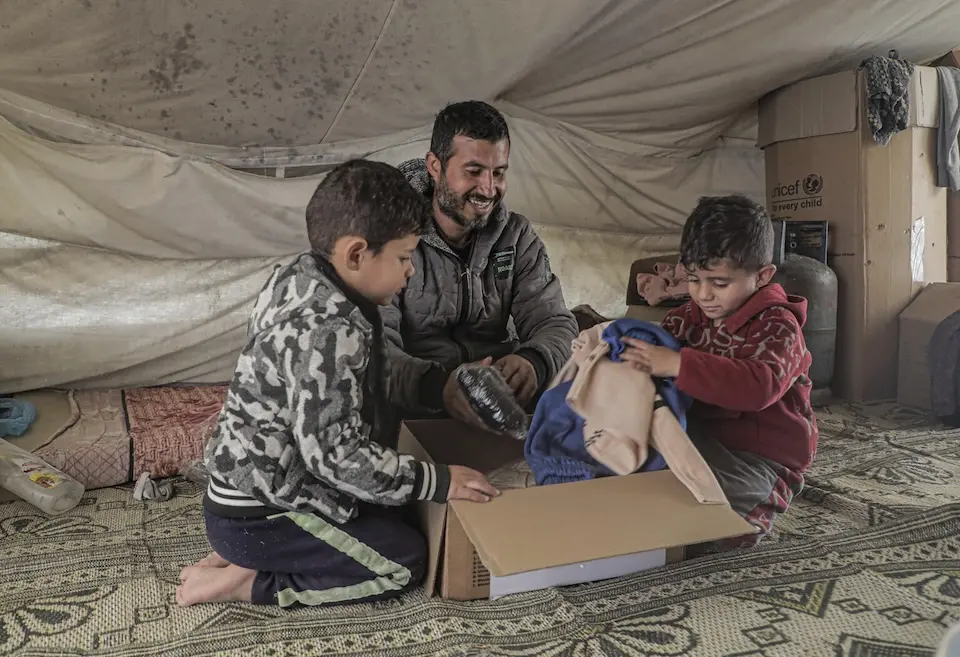 A displaced Palestinian family unpacks a box of warm winter clothes distributed by UNICEF and partners in the Gaza Strip.