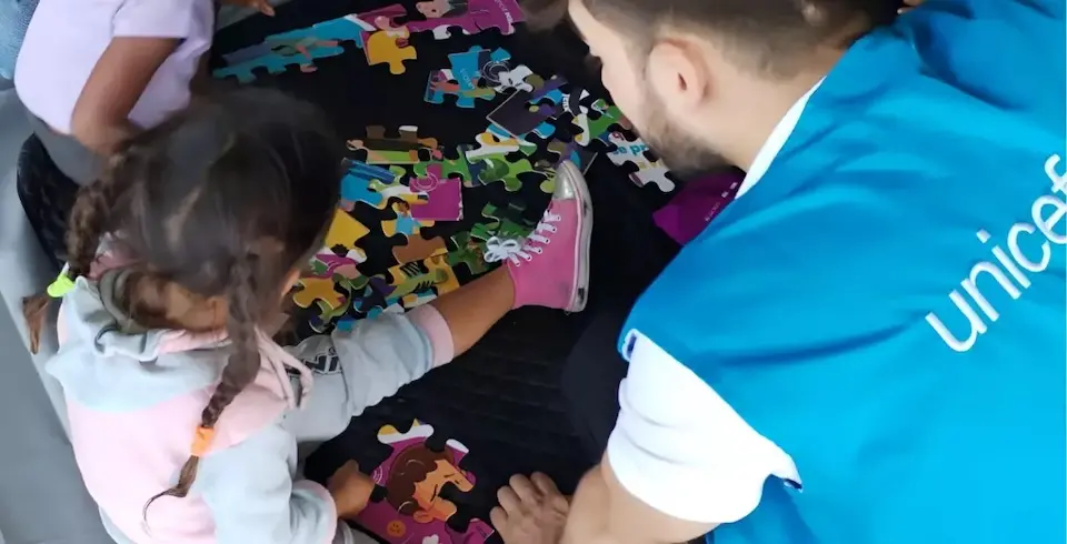 A UNICEF staff member sits on the floor with children at a child-friendly space established as part of a violence prevention initiative in northern Medellín, part of a larger humanitarian assistance program for children and families in transit.