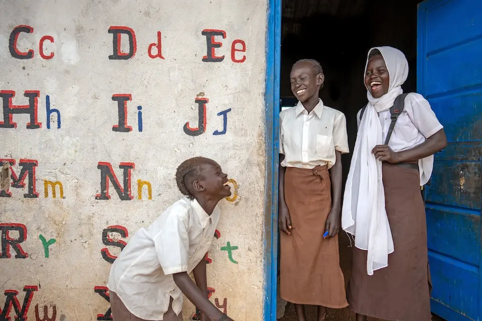 Three students smile at each other while standing in the doorway of a UNICEF-supported school in Renk, north South Sudan.