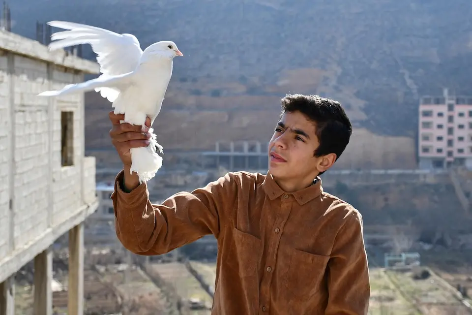 On Feb. 2, 2025, Mohammed, 15, gently holds a bird he raised on the roof of his home in Bseimeh village, Rural Damascus, Syria.