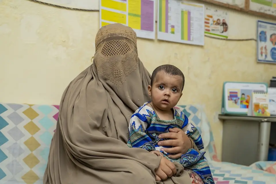 Mother holding infant daughter at health clinic in Islamabad
