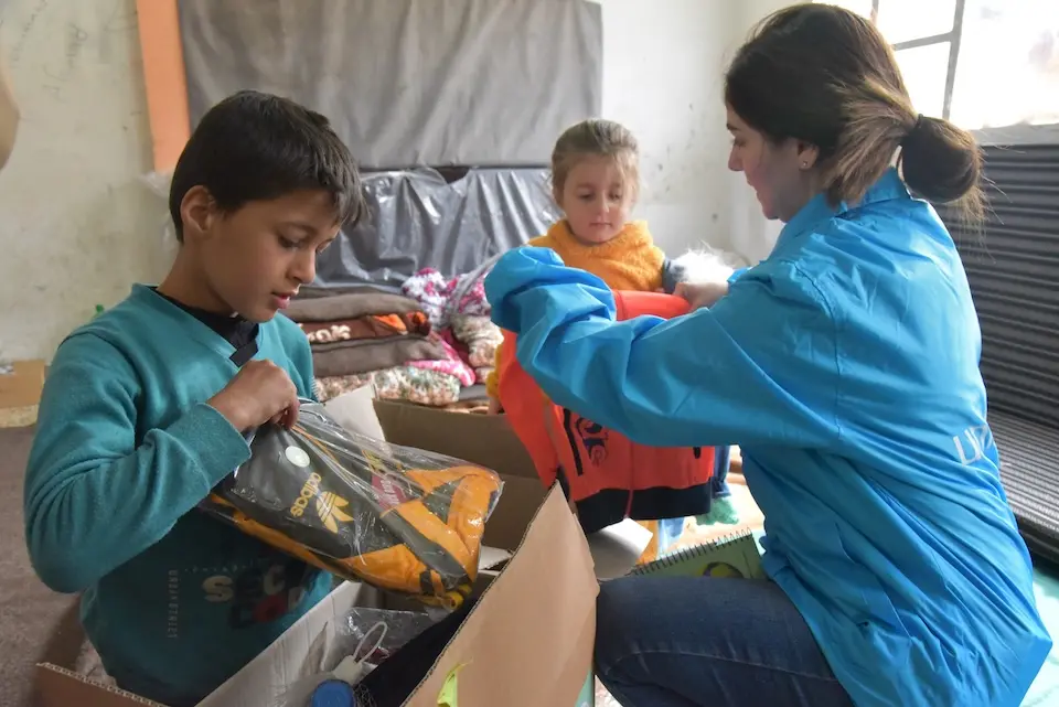 Two children receive warm clothes distributed by UNICEF at a school-turned-shelter for displaced families in Naher Al Bared village, rural Hama, Syria.