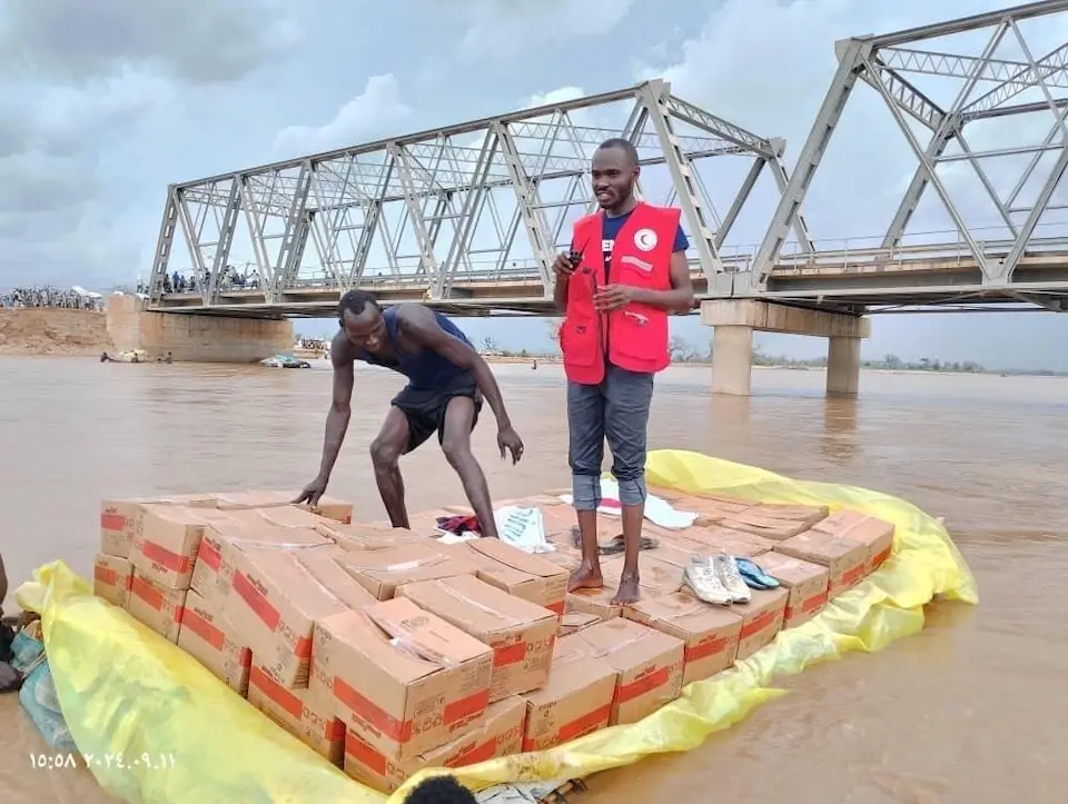 UNICEF partners and volunteers transport cartons of ready-to-use therapeutic food across Wadi Mornei bridge in Sudan after it was destroyed by floods.