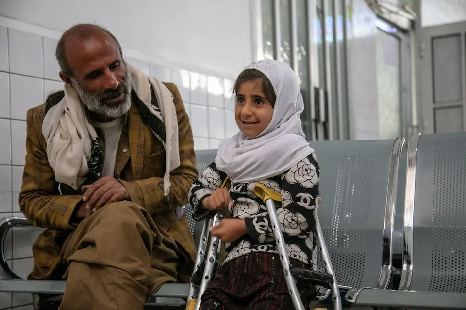 Khadija, 9, and her father sit together telling jokes as they await the fitting of her prosthetic limb at the Prosthetic Center in Sana’a Governorate, Yemen.