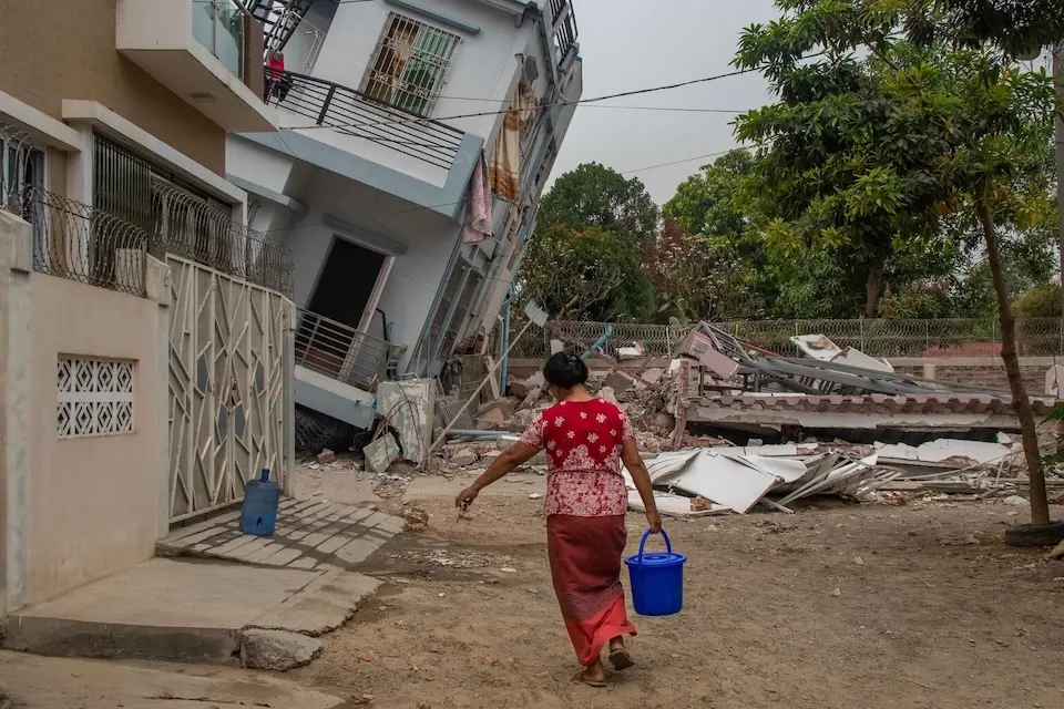 On April 6, 2025, a woman carries a blue bucket filled with drinking water provided by UNICEF in Oo Yin Kone ward, Aung Myay Thar Zan township, Mandalay region, Myanmar.