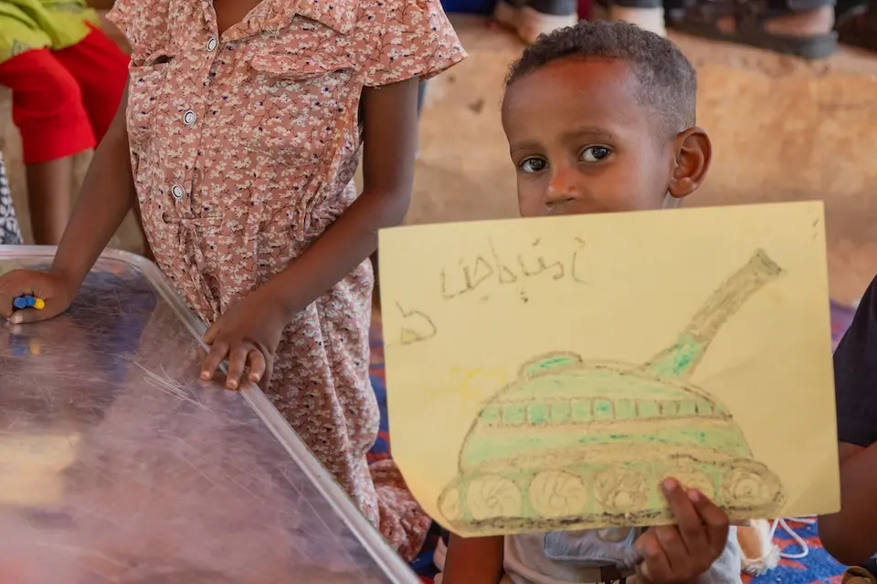 On April 5, 2025, a child shows his drawing of a tank at a UNICEF-supported child-friendly space (CFS) in the Alhatana neighborhood, Omdurman, Khartoum State, Sudan.