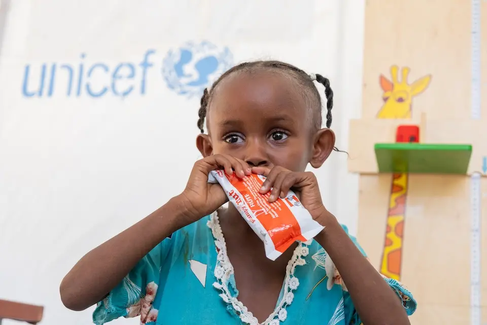 At a Sudan clinic, a young girl with severe acute malnutrition eats from a packet of ready-to-use therapeutic food supplied by UNICEF.