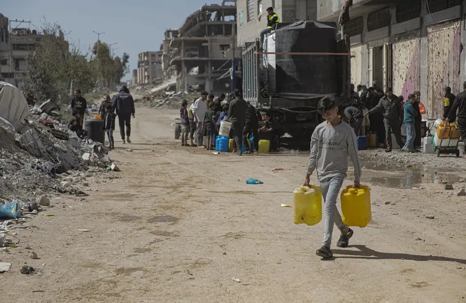On March 24, 2025, a child carries water containers back to his tent in Beach Camp, Gaza City, after filling them from tanks of safe water brought by UNICEF trucks.
