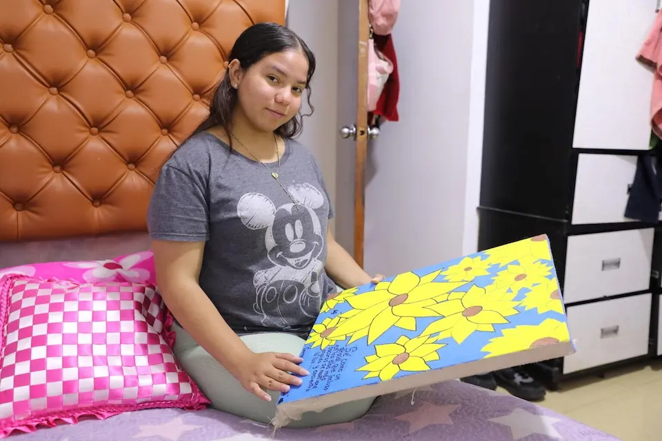 A teenager from Venezuela holds a painting she made in her new home in Peru. 