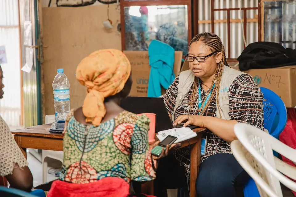 UNICEF staff person sits with beneficiary of cash assistance in South Kivu province, DRC.