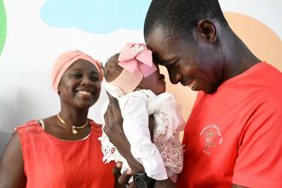 A smiling father holds his infant daughter in his arms in Côte d'Ivoire.