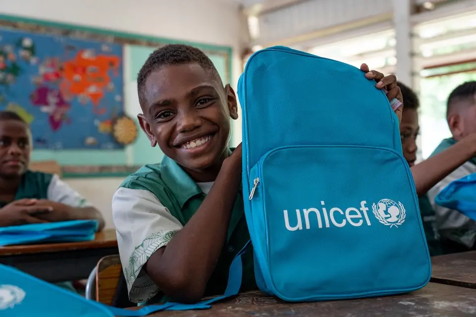 A young student in Vanuatu smiles at school with a UNICEF-provided backpack