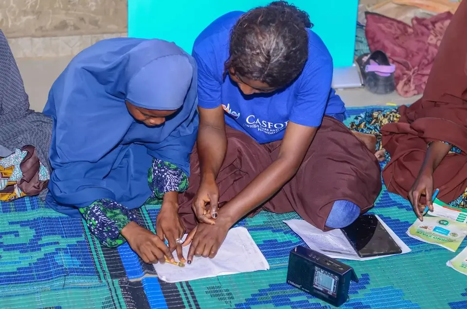 A teacher helps a student using radio lessons in Maiduguri, Nigeria.