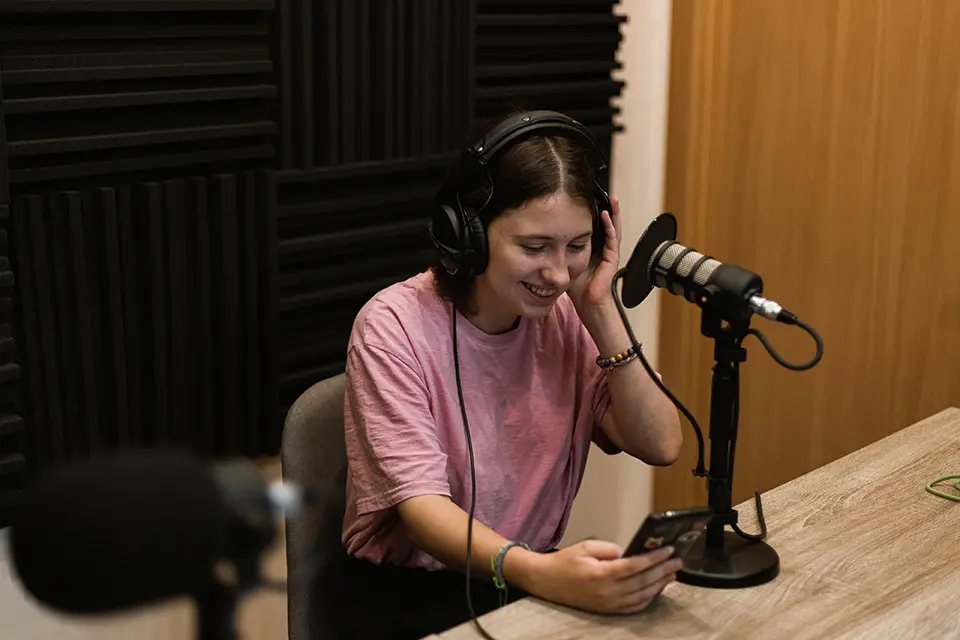 Young woman wearing headsets, looking at her phone screen and sitting behind a microphone