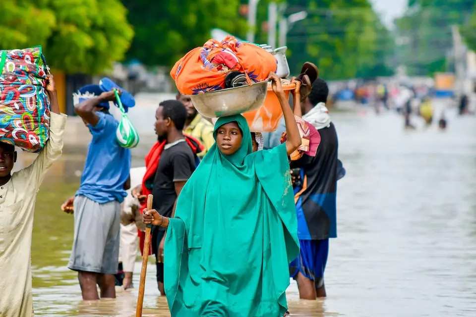 People carry their belongings on their heads as they walk through floodwaters in northeastern Nigeria in 2024.