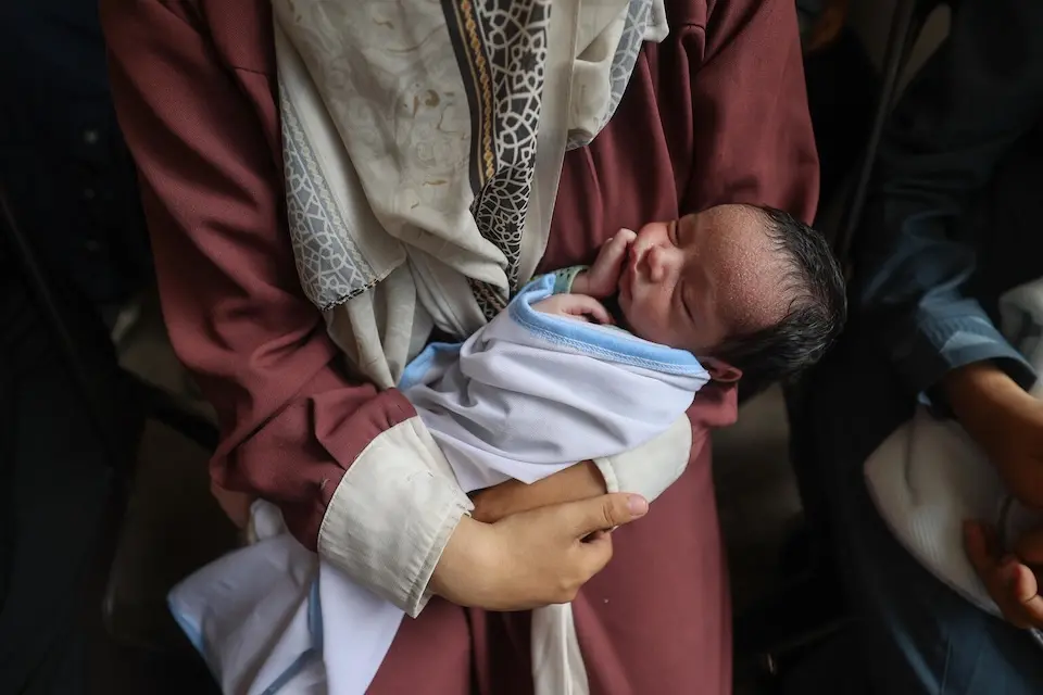 A mother holds her baby on her lap as they wait to be seen for a nutrition screening in central Gaza.