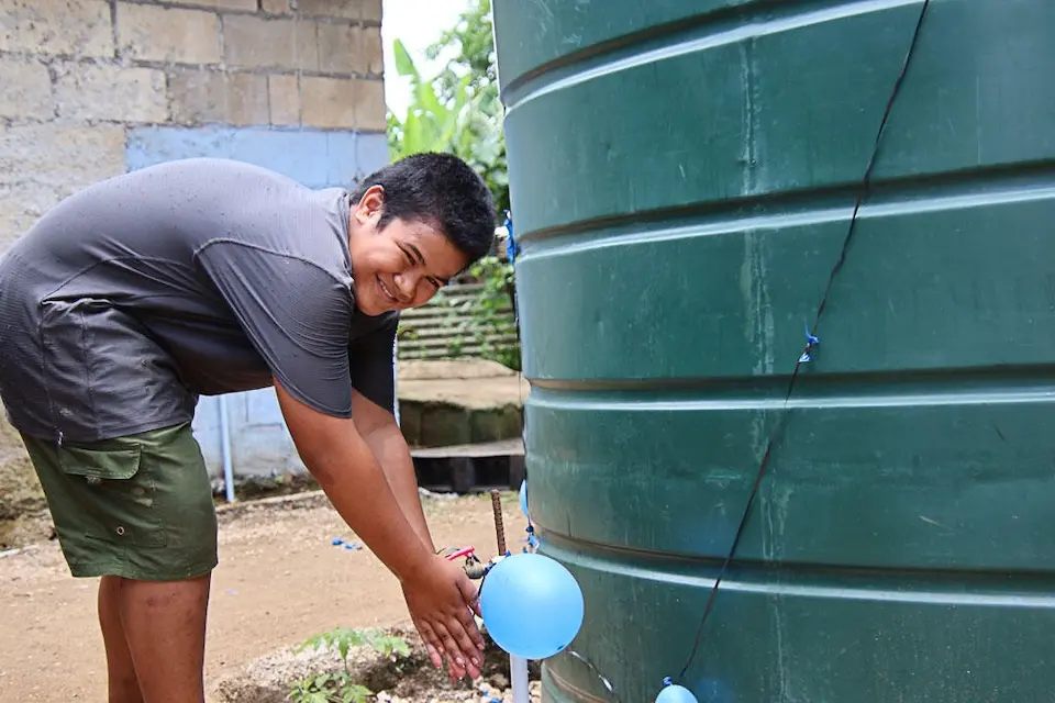 A 12-year-old boy washes his hands using a UNICEF-supported water tank at home in Tofoa, Tonga.