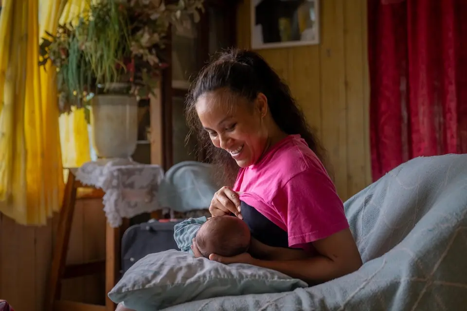 A mother feeds her baby during a home visit with a community health worker in Tonga.