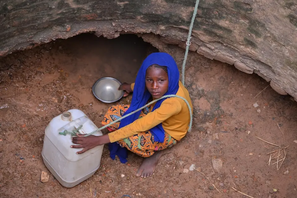 A 12-year-old girl scoops water from a spring at the bottom of a deep well in rural Al-Serif village, Central Darfur, Sudan.