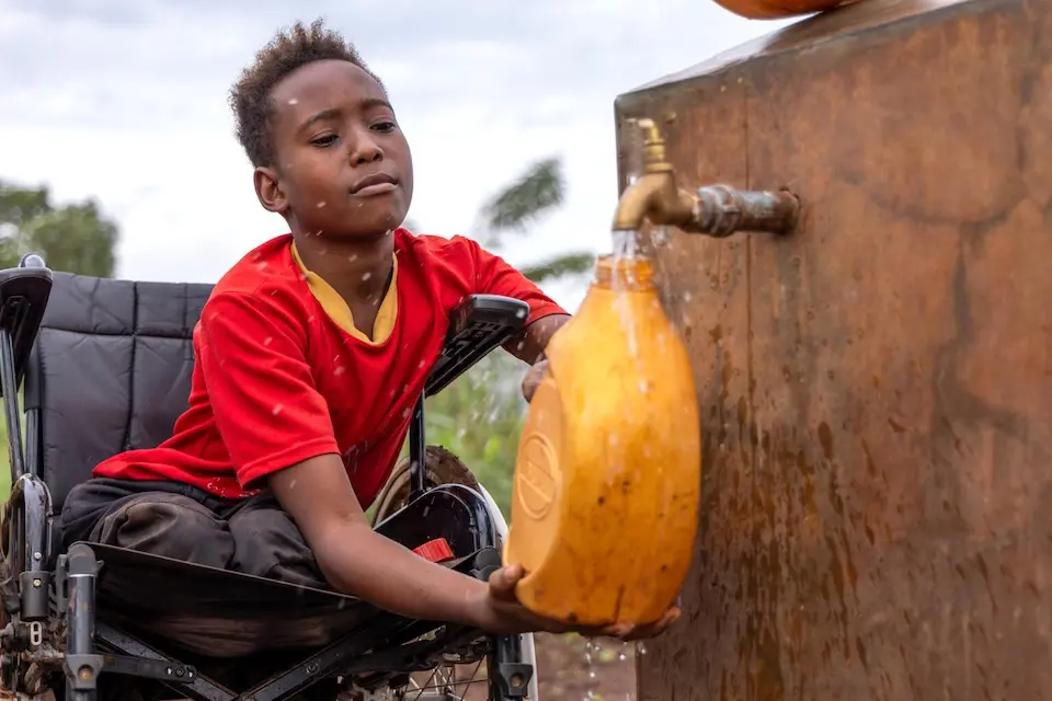 In a Ugandan village, a boy in a wheelchair fills a jerry can with clean water from a UNICEF-supported access point.