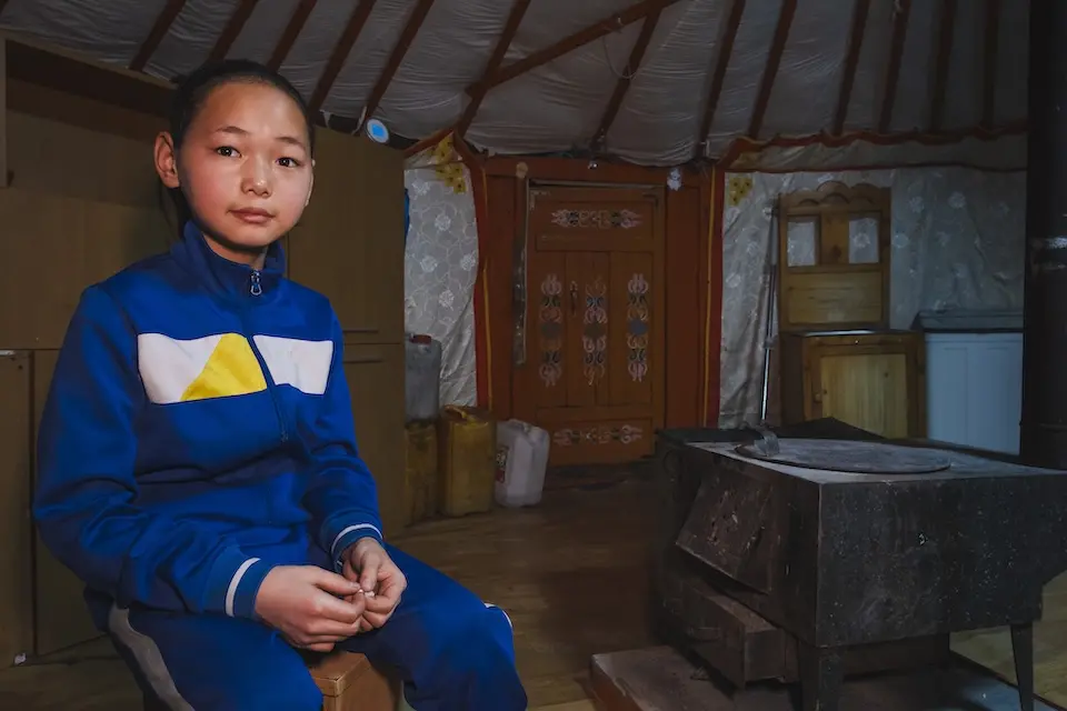 Young girl seated next to coal burning stove in traditional Mongolian home, or ger