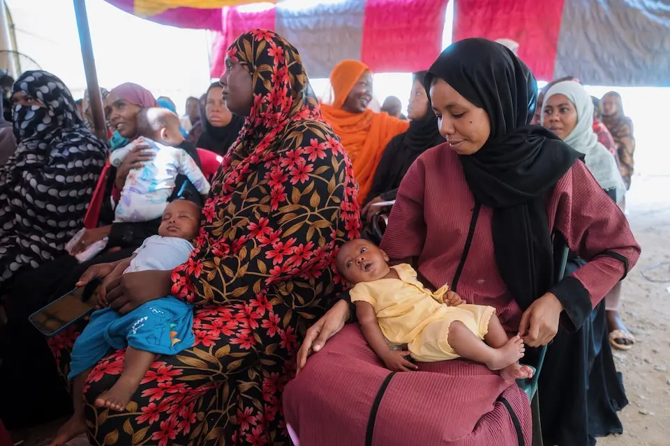 At a primary health center in Port Sudan on Aug. 7, 2025, two mothers, babies in their laps, register for UNICEF humanitarian cash support. 