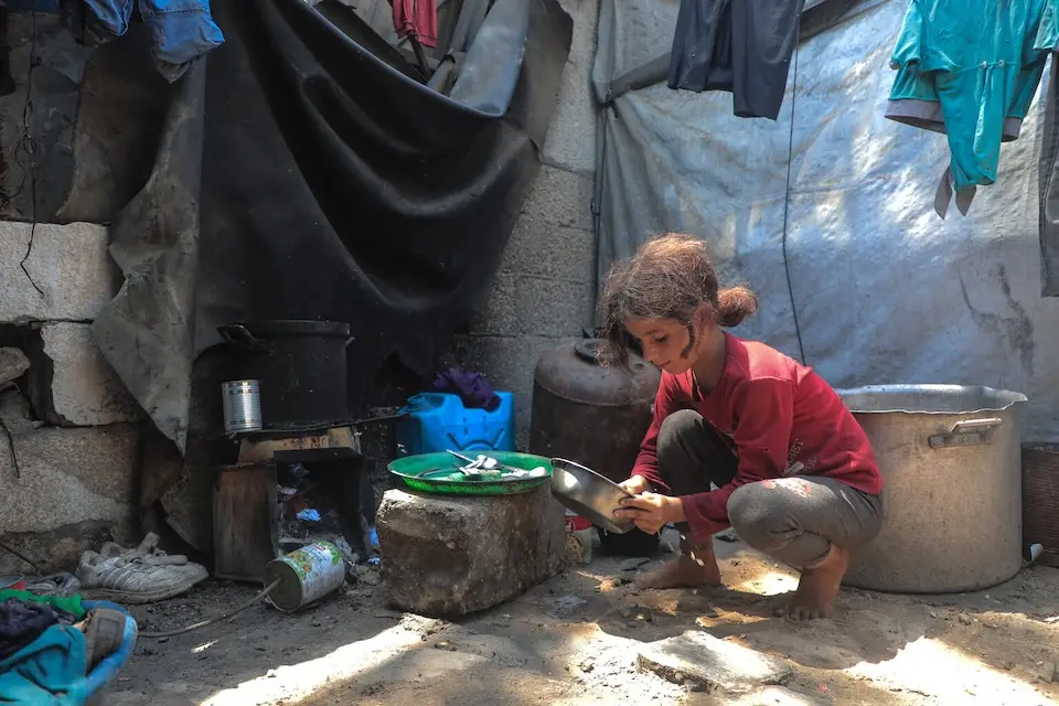A 10-year-old girl crouches down to clean a dish in her family's outdoor cooking area in Gaza.